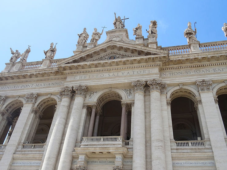 Facade of the Basilica di San Giovanni in Laterano in Rome, featuring grand columns and statues on the roof against a blue sky.
