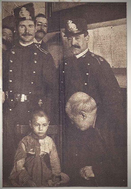 Historical photograph featuring two police officers in uniforms standing with two young children, one sitting on a chair and the other kneeling beside them, set in an old interior, possibly related to the child abduction cases in early 20th century Barcelona.