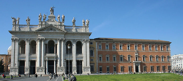 A view of the Basilica di San Giovanni in Laterano, showcasing its grand façade and surrounding lawn in bright daylight.