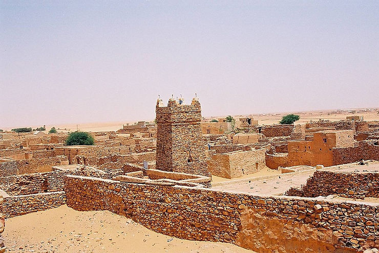 A view of ancient structures in the Sahara, showcasing traditional architecture with stone walls and a prominent tower under a clear blue sky.